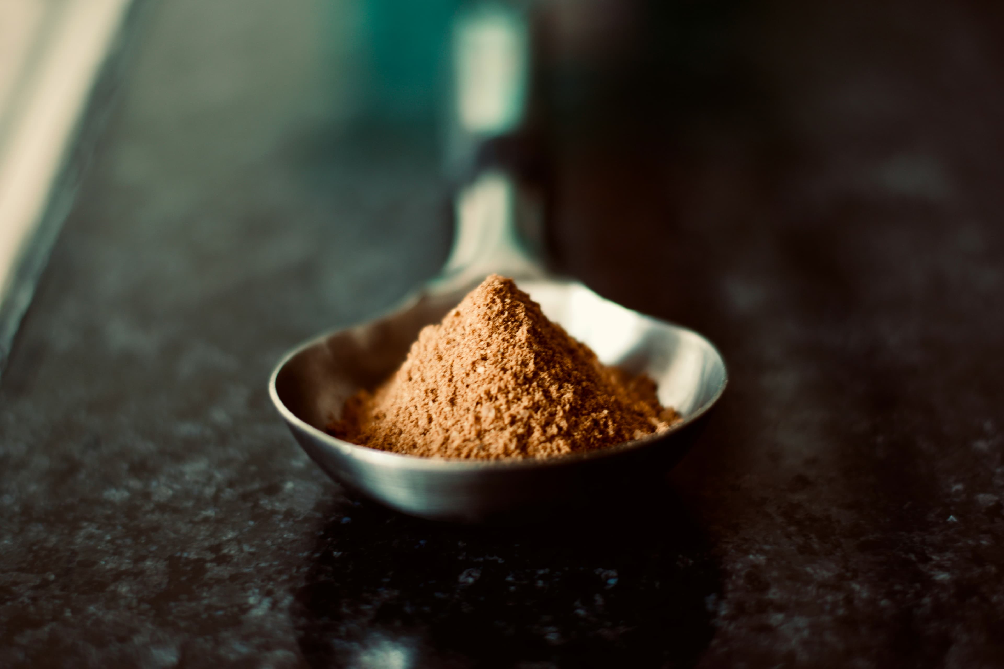 Spoonful of fine brown botanical or nutritional powder for ingredient trade.